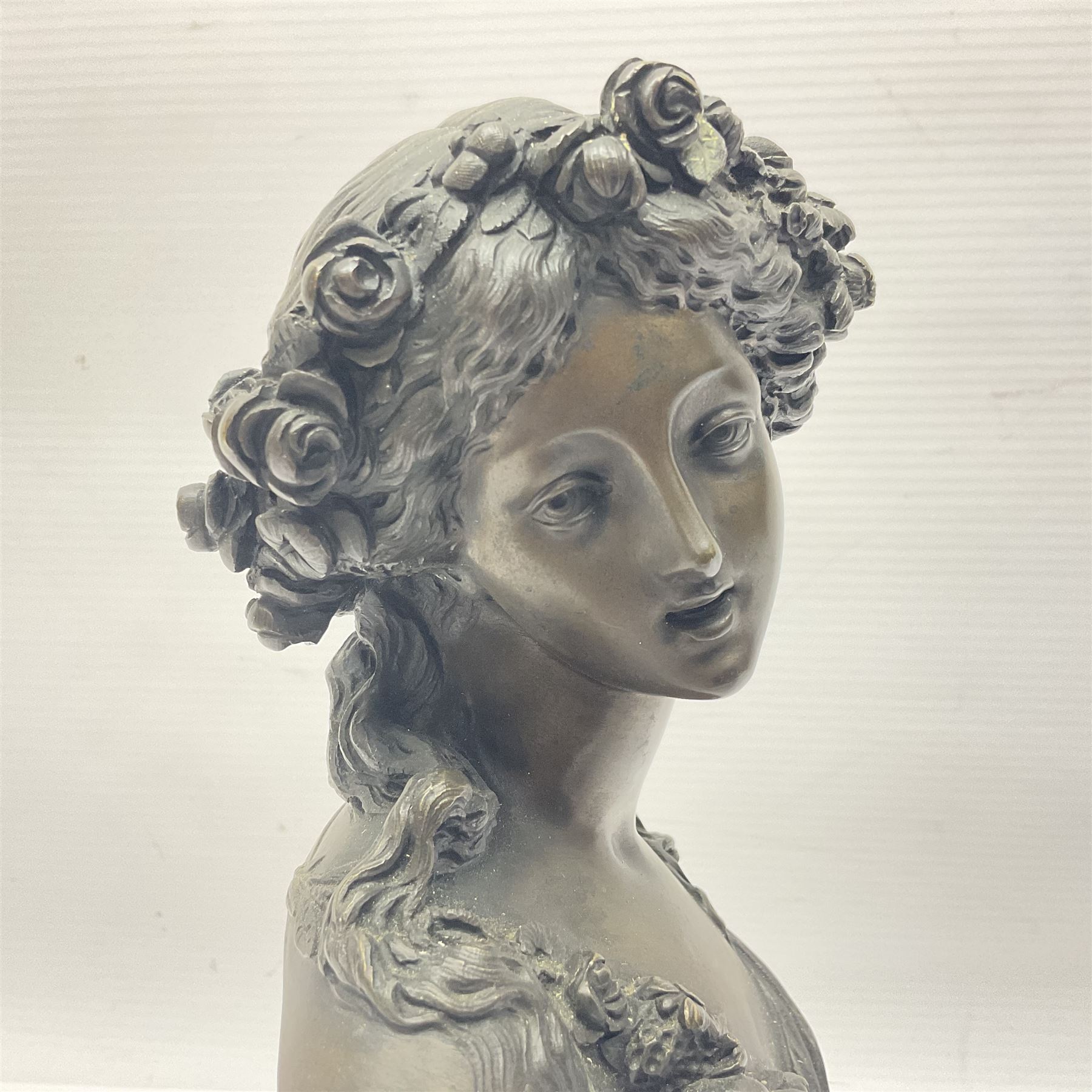 Bronze bust, modelled as a maiden in classical drapery and adorned with floral swags, upon a fluted socle base, overall H23.5cm