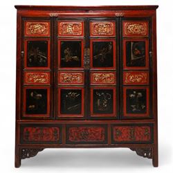 19th century Chinese red and black lacquered hardwood cabinet fitted with four panelled doors, the frieze decorated with scrolling gilt patterns over gold bat mounts surmounting the hinges, the black panels depicting traditional figural and floral scenes, the carved parcel-gilt panels with pagoda, pastoral and war scenes, the doors fitted with metal fish and pagoda handles, enclosing a single shelf and four internal drawers, the base compartment decorated with carved precious objects, raised on moulded square supports with pierced scrolling brackets