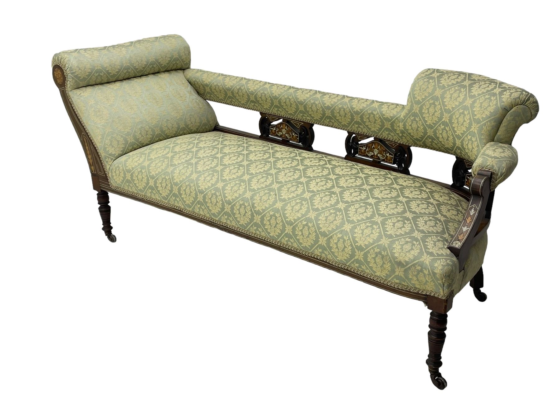 Late Victorian walnut salon settee or chaise lounge, double-ended with rolled back and curved end, upholstered in light aquamarine fabric with raised repeating lozenge pattern, decorated with laurel leaf wreaths and urns, three pierced splats carved with curled leaves, inlaid with dolphins and scrolled foliate motifs in simulated ivory and boxwood, on tapering ring turned supports with brass and ceramic castors (L166, D60, H70cm); together with matching tub-shaped armchair (W61cm, H73cm, D66cm)  