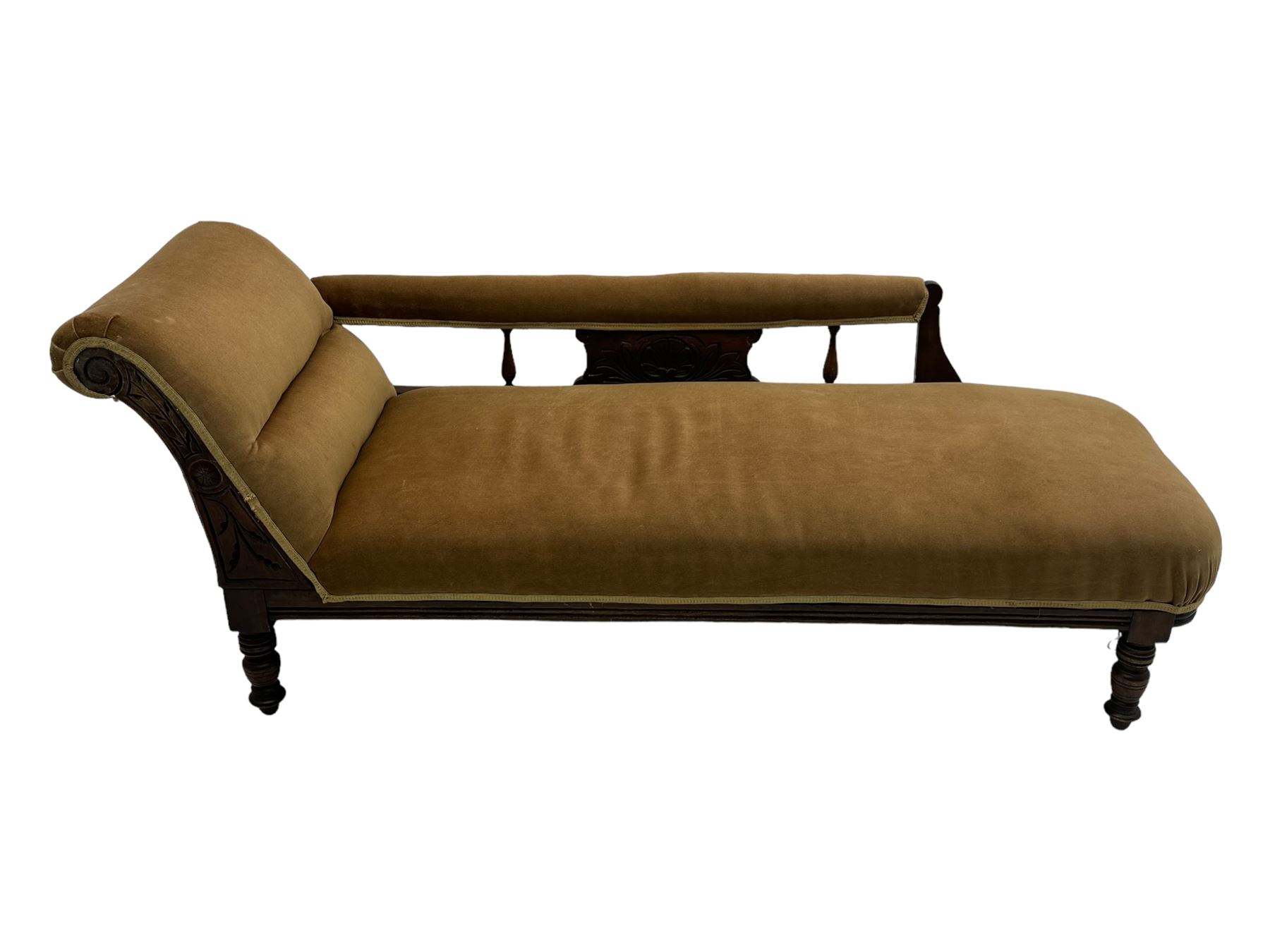 Late 19th century mahogany framed chaise longue, upholstered in tan fabric, featuring scrolled backrest with carved floral motifs, supported by turned legs