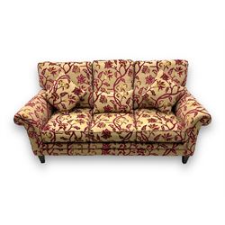 Contemporary upholstered three-seat sofa, scroll arms and loose cushions, embossed beige ground fabric with red and gold floral motifs, on tapered wooden supports