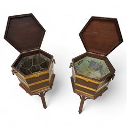 Pair of George III mahogany and brass bound cellarettes or wine coolers on stands, hexagonal form, moulded hinged lid enclosing metal lining, the body strapped in brass bands and fitted with carrying handles, the stand with moulded upper rails on splayed and moulded square supports with castors, with arched corner brackets 