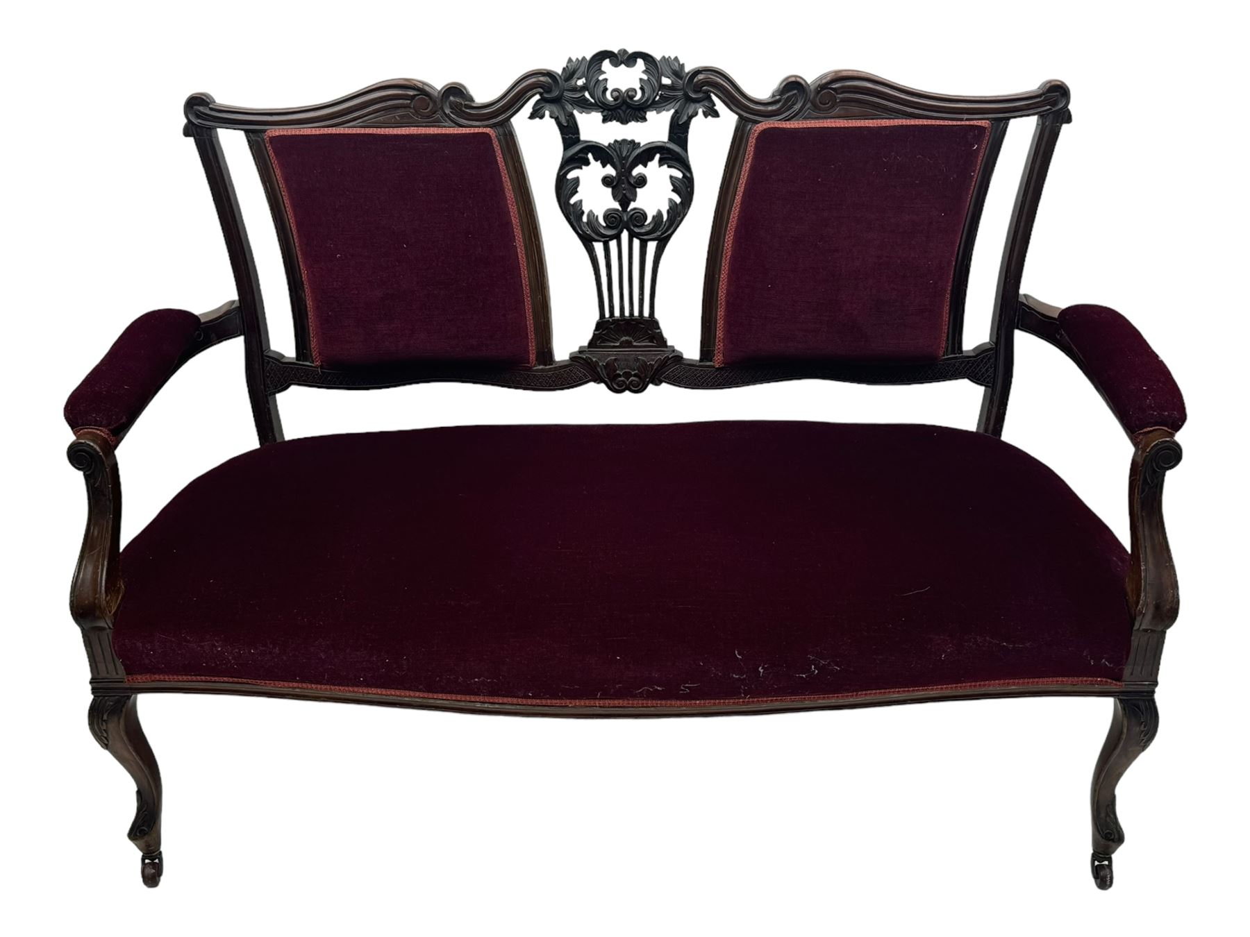 Late Victorian dark oak framed sofa, the backrests, seat and padded arms upholstered in deep red fabric, carved crest rail with scroll and foliate motifs supported by carved uprights, on cabriole supports with leaf carvings terminating in castors