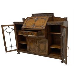 Early 20th century heavily carved oak bookcase bureau, raised back with grape-vine carved frieze, over fall-front enclosing fitted interior, above two short drawers and curved frieze drawer, flanked by astragal glazed and panelled cupboards, on turned feet