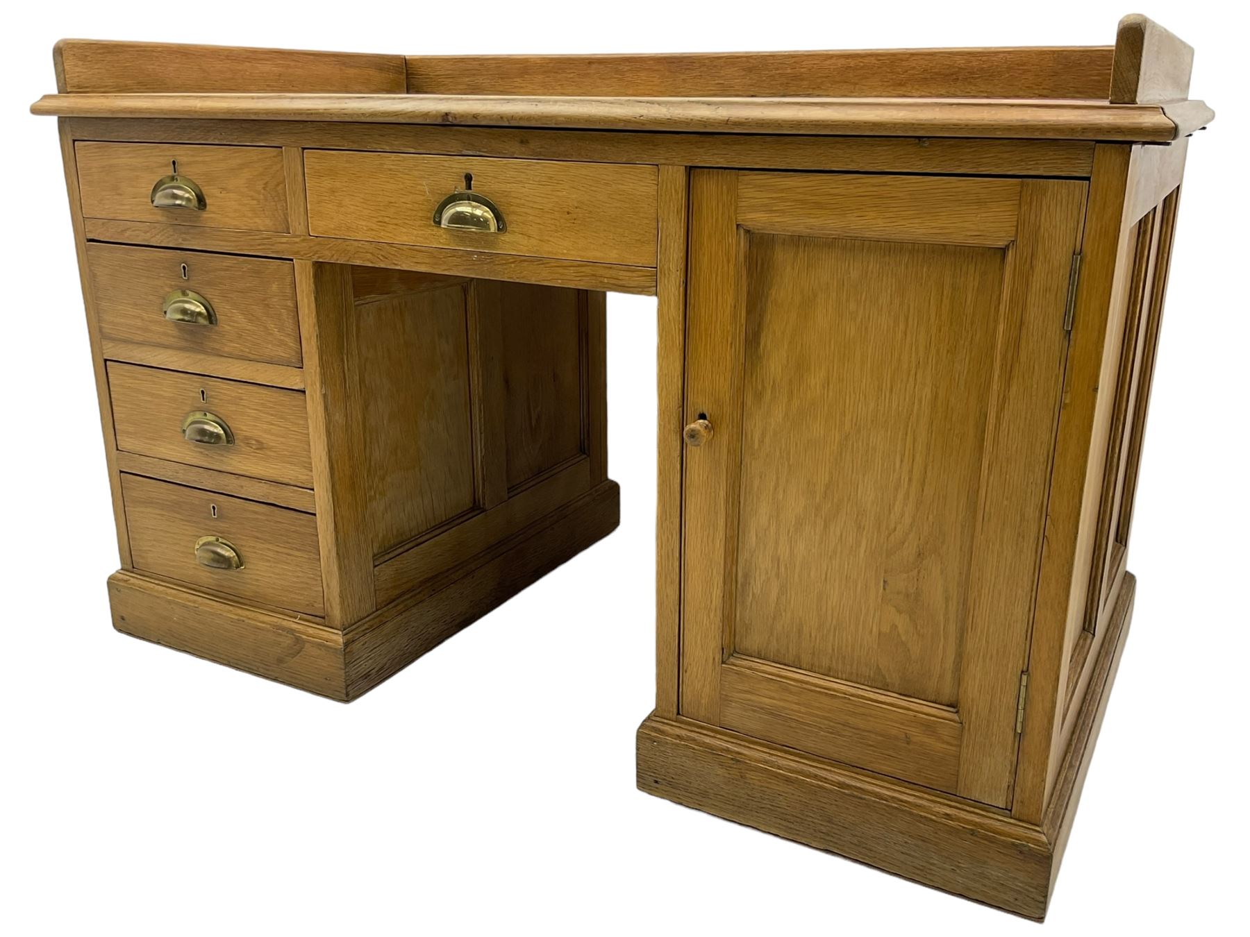 20th century oak desk, moulded rectangular top with raised back and inset leather writing surface, fitted with five drawers and single panelled cupboard, on moulded plinth base