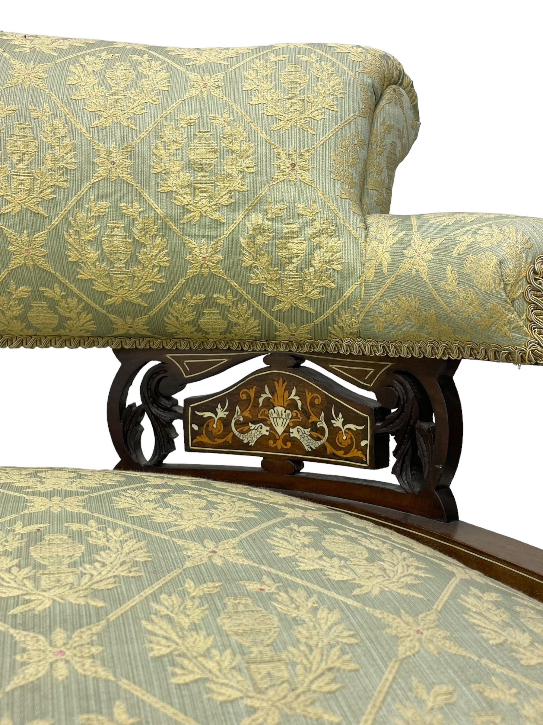 Late Victorian walnut salon settee or chaise lounge, double-ended with rolled back and curved end, upholstered in light aquamarine fabric with raised repeating lozenge pattern, decorated with laurel leaf wreaths and urns, three pierced splats carved with curled leaves, inlaid with dolphins and scrolled foliate motifs in simulated ivory and boxwood, on tapering ring turned supports with brass and ceramic castors (L166, D60, H70cm); together with matching tub-shaped armchair (W61cm, H73cm, D66cm)  