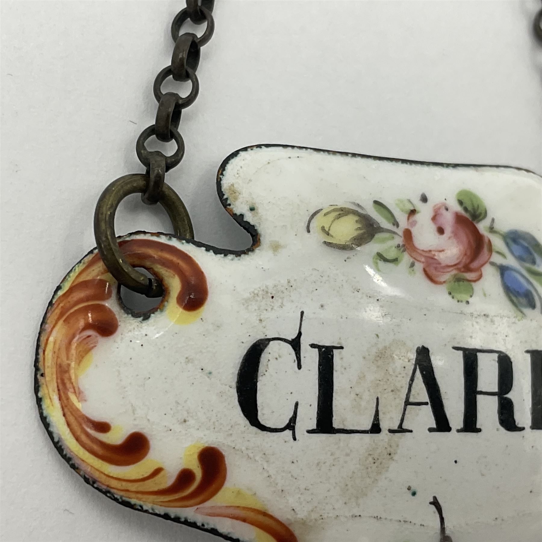 Two late 18th/early 19th century enamel wine labels, each of shaped form, titled 'CLARET', and 'SHERRY' and decorated with floral sprigs and scroll detail upon a white ground, each with suspension chain, each approximately H3.5cm W5cm