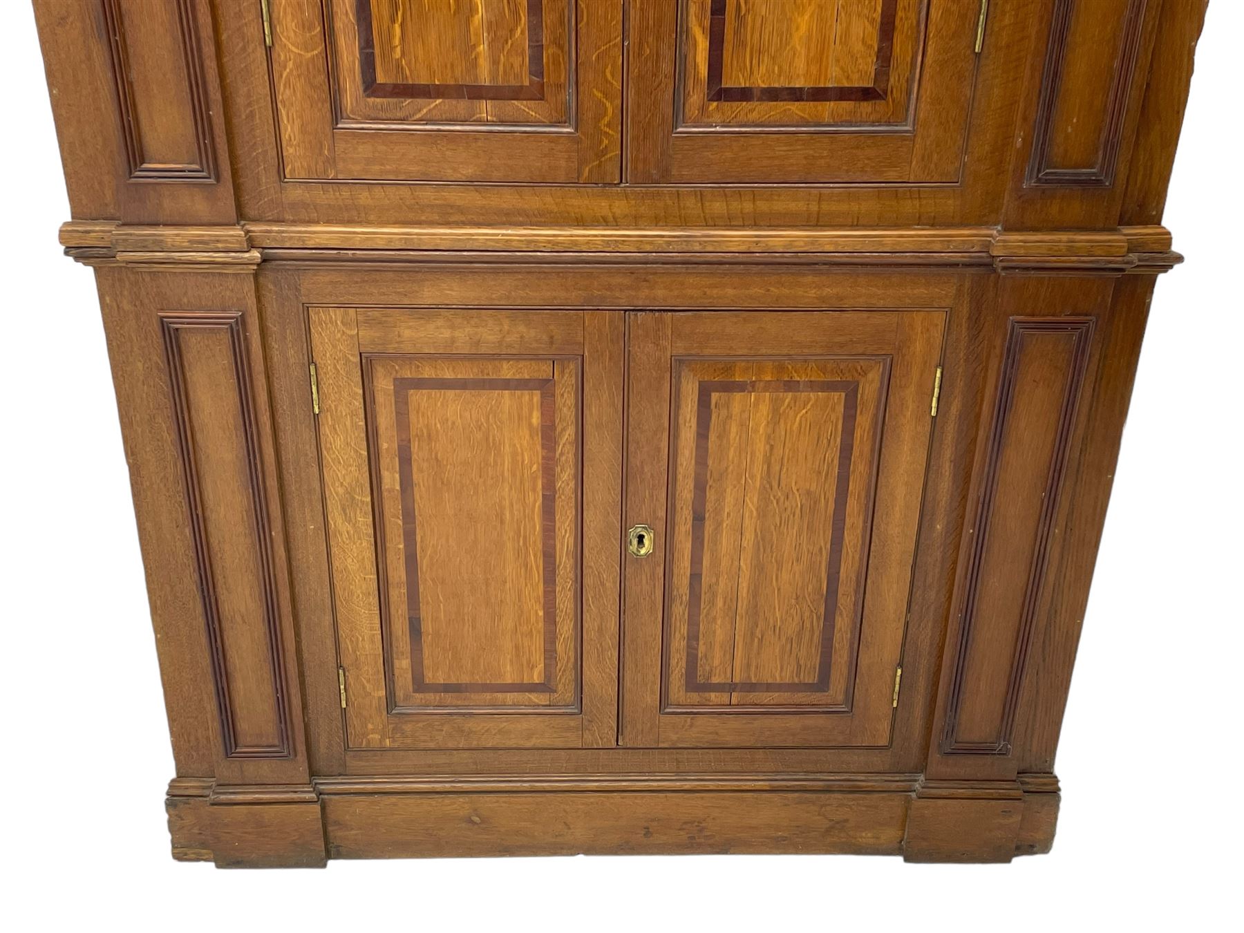 George III and later oak and mahogany banded corner cupboard, moulded cornice over four panelled doors, the door panels inlaid with mahogany bands, projecting square pilasters throughout with applied reeded mouldings, the painted interior fitted with shaped shelves, on moulded plinth base 