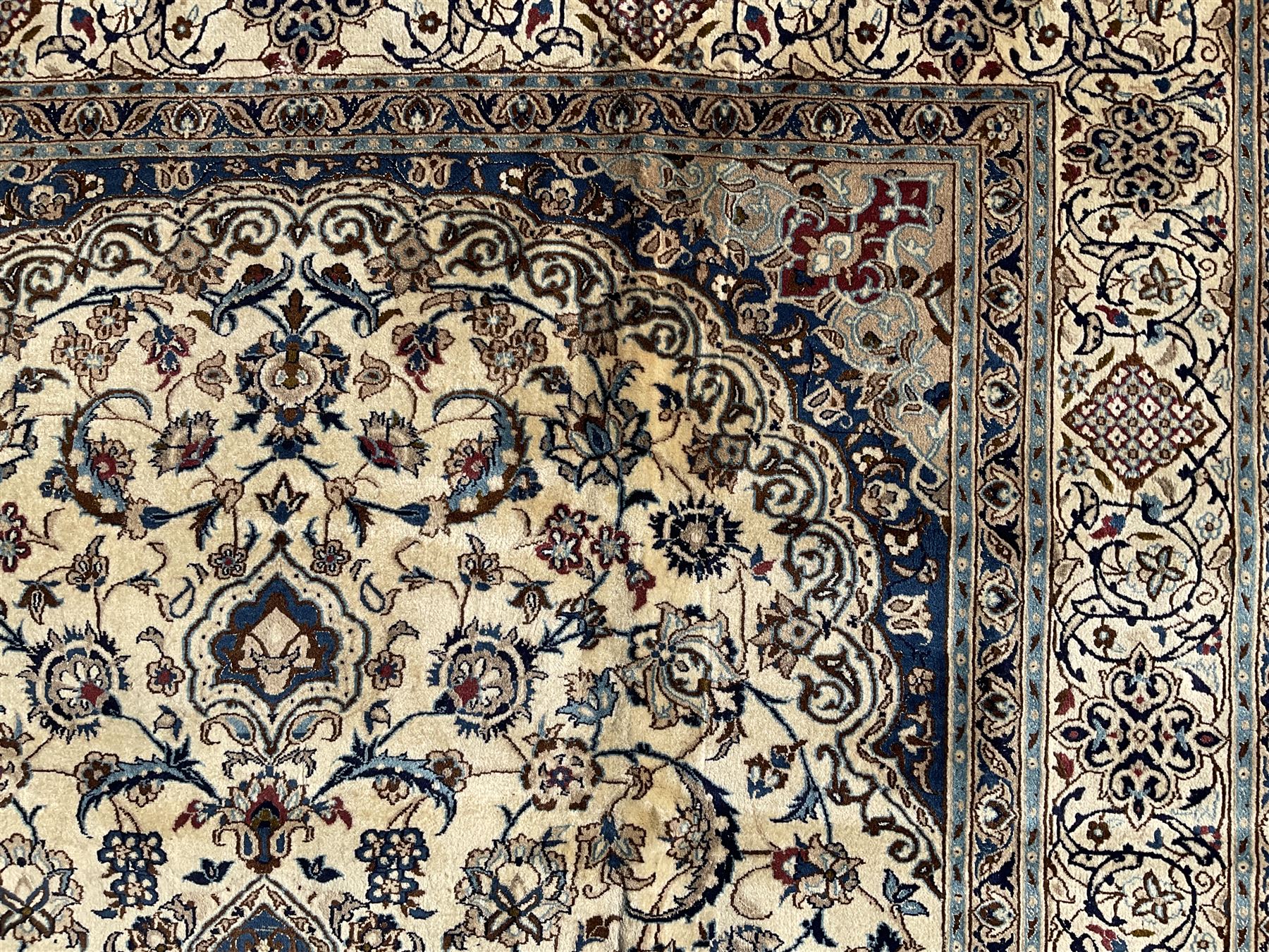 Persian Nain ivory ground carpet, central indigo medallion, the busy floral field decorated with scrolling vines and flower heads in shades of blue, beige, and red, wide guarded border with repeating palmettes and foliate motifs