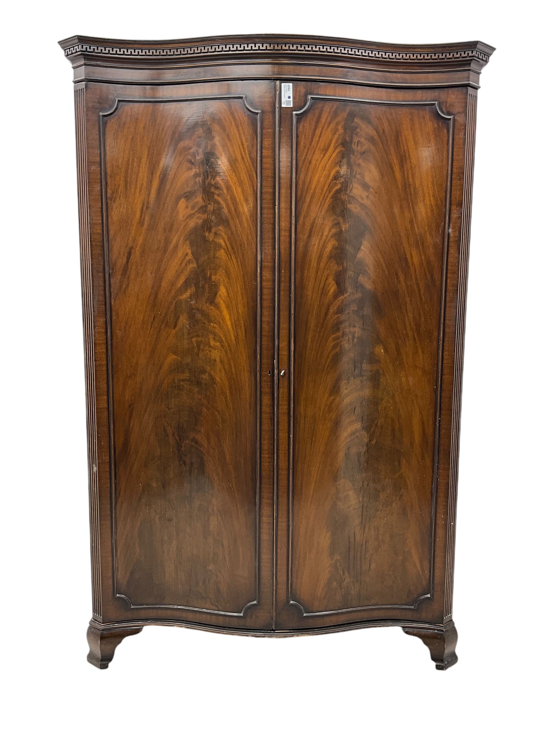 Early 20th century mahogany serpentine double wardrobe, moulded cornice over two figured doors, the interior fitted with hanging rail and shelf, canted and fluted uprights, on bracket feet 