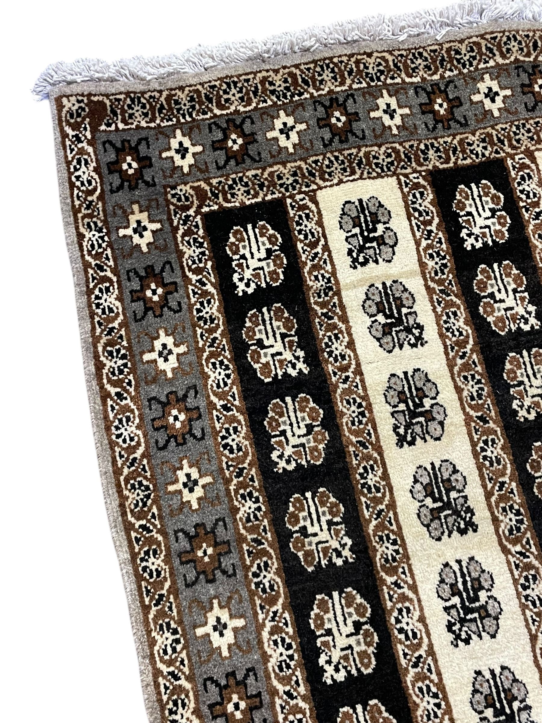 Persian ivory ground rug, the field divided into stripes decorated with stylised flower heads, the border with repeating cross motifs within guard stripes 