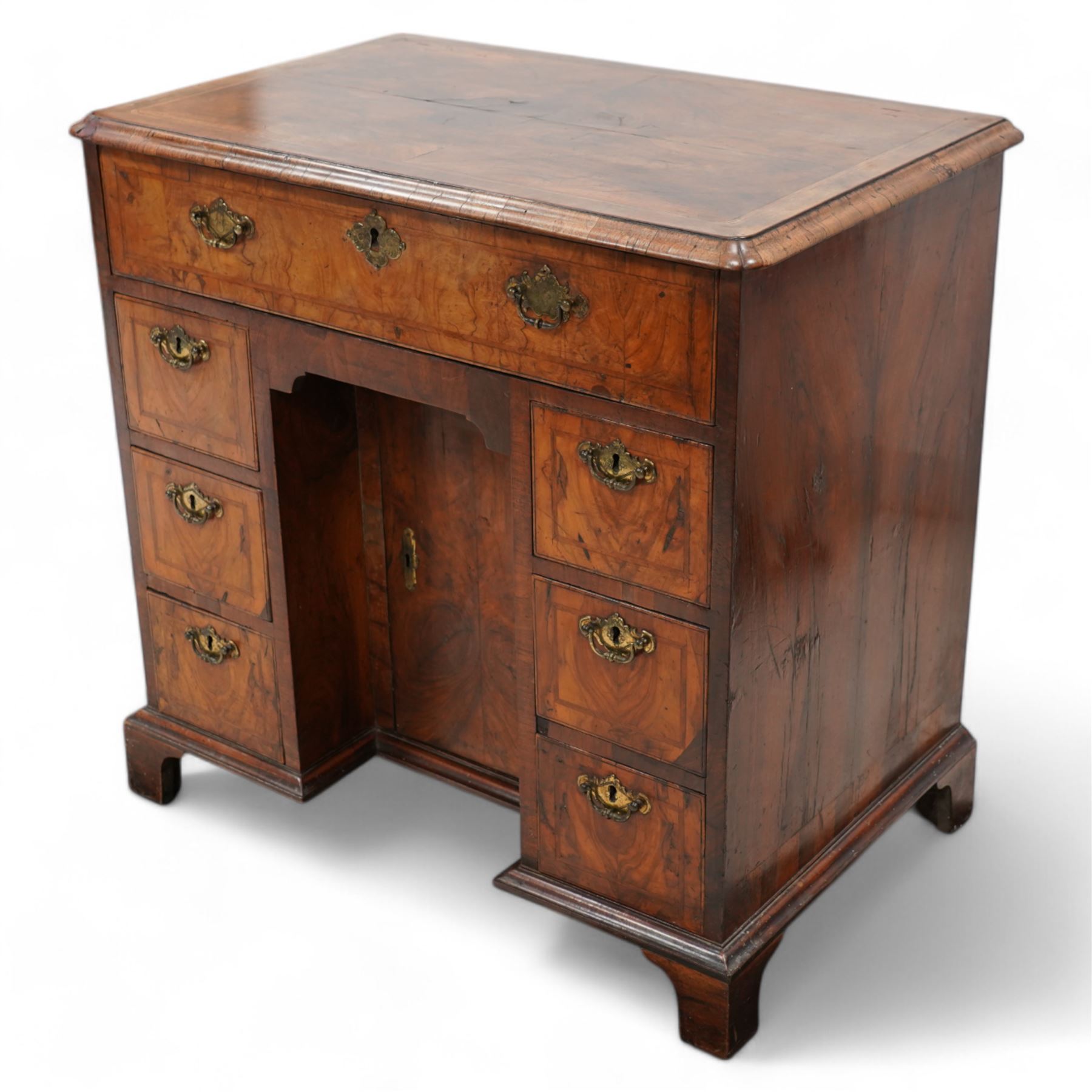 George II figured walnut knee-hole desk, the rectangular quarter-matched veneer top with moulded edge, crossbanding and feathered-banding, fitted with single frieze drawer over three drawers to each side, each with the central recess fitted with a single cupboard enclosing shelf, lower moulded edge on bracket feet