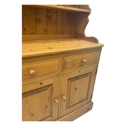 Large traditional pine dresser, shaped cornice over three open shelves, base fitted with four drawers above four panelled cupboards, each with turned wooden knobs, on plinth base