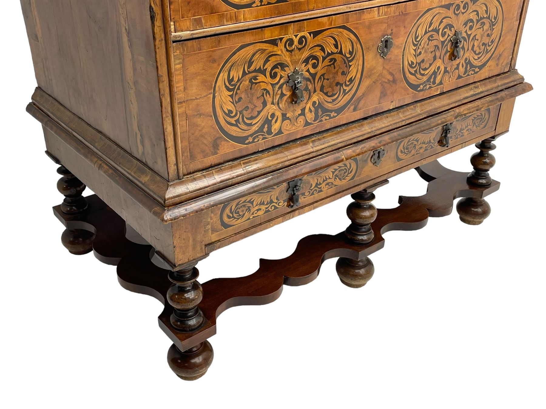 18th century inlaid walnut chest on stand, ovolo-moulded rectangular top inlaid with ebony panels each decorated with scrolling foliage, flower heads and birds, fitted with two short over three long drawers, the drawer fronts decorated with ebony panels enclosing curled leaf inlays, the base fitted with single drawer on turned supports united by waved stretchers, on turned bun feet 