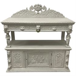 Victorian white painted heavily carved oak buffet, shaped pediment decorated with central urn filled with fruit flanked by winged beasts and scrolling acanthus leaves, moulded rectangular top carved with foliage, two drawers with Greenman mask handles over undertier, the upper tier supported by flute playing musicians, the lower section fitted with cupboard enclosed by panelled door carved with tavern scene, bead carved lower mouldings, on stile supports 