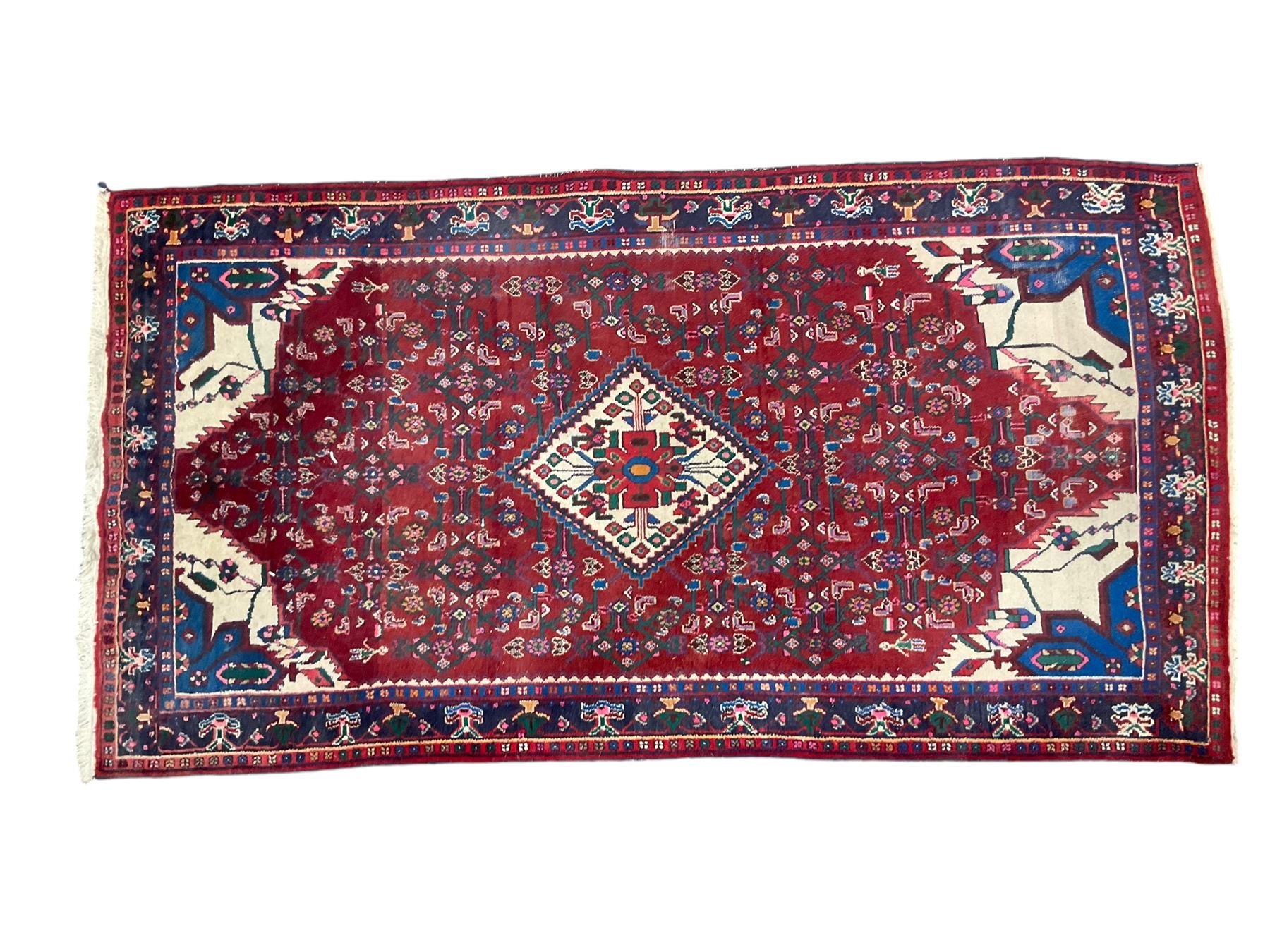 Persian Herati crimson ground rug, the busy field decorated with a central lozenge medallion surrounded by interlocking Herati motifs, the indigo guard band with repeating palmette and stylised plant motifs