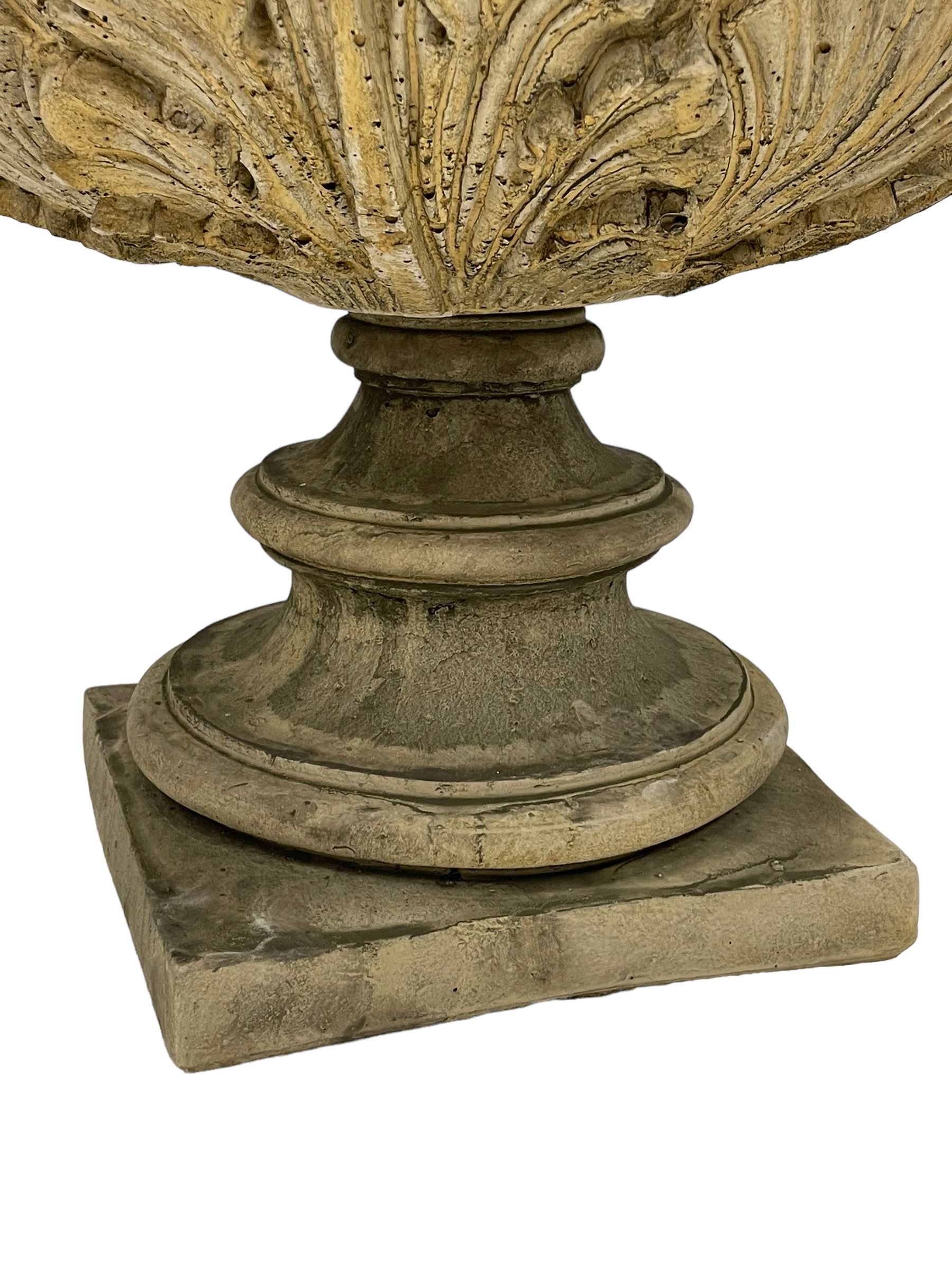 Pair of composite stone garden urn planters, acanthus leaf garland rim over foliate decorated body, stepped foot on square base