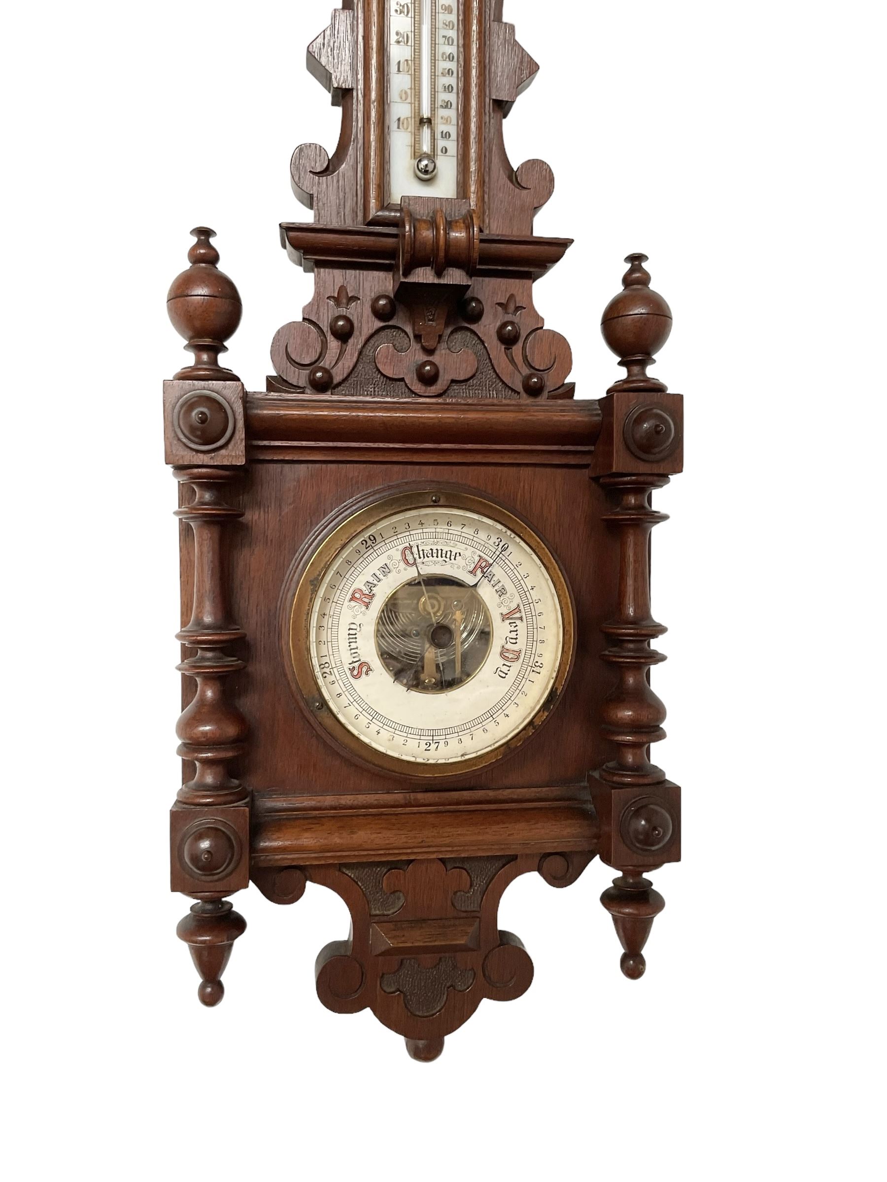 Early 20th century Edwardian aneroid barometer, in a mahogany case with scroll carving, turned finials and pendants, boxed mercury thermometer recording temperature in degrees Fahrenheit and centigrade on opaline register, open dial barometric register with gothic script predictions, steel indicating hand and brass recording hand.