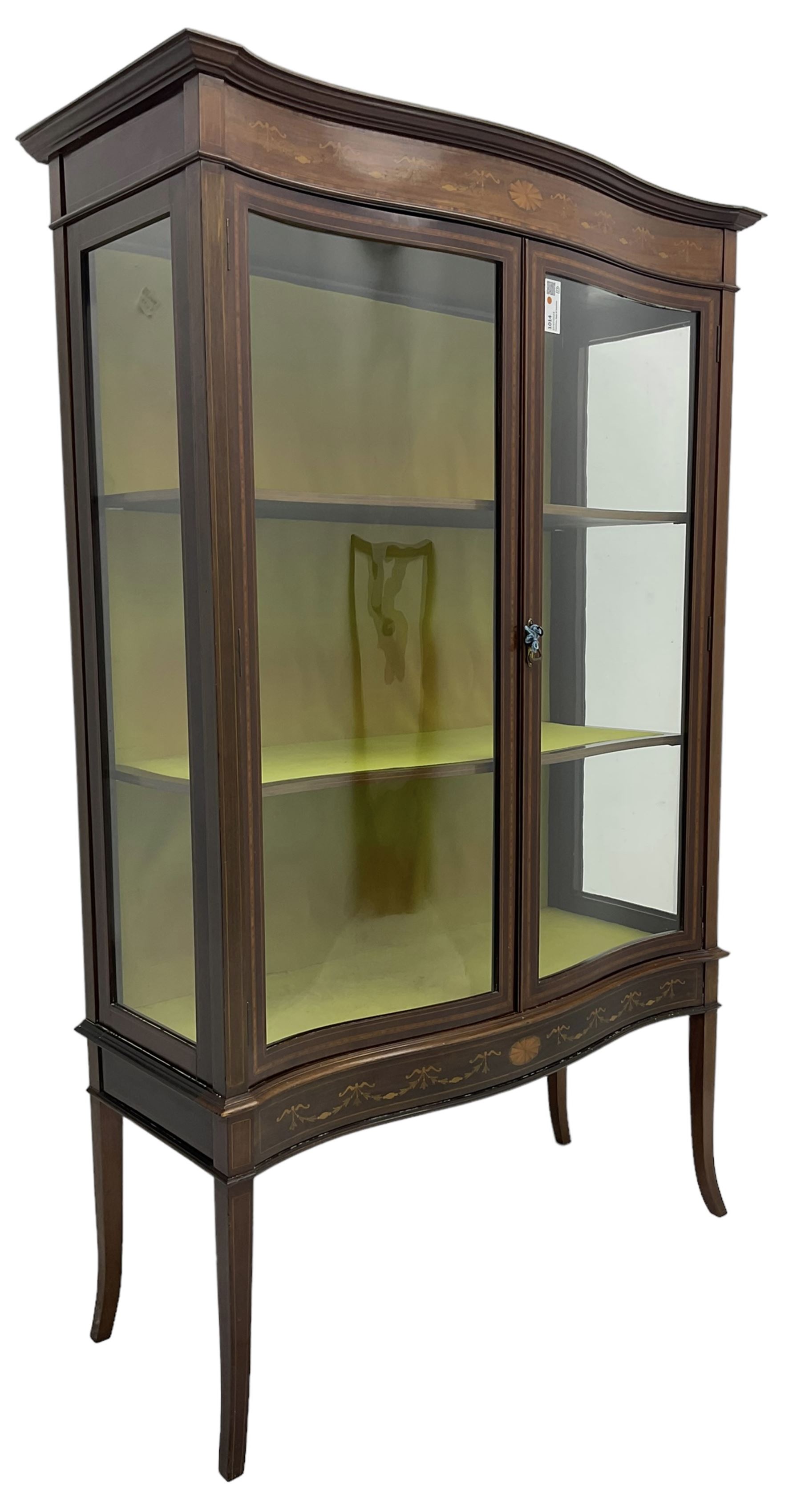 Edwardian inlaid mahogany serpentine display cabinet, projecting moulded cornice over figured frieze inlaid with tailing bellflowers and central fan motif, enclosed by two glazed doors, on square tapering supports with splayed terminals 