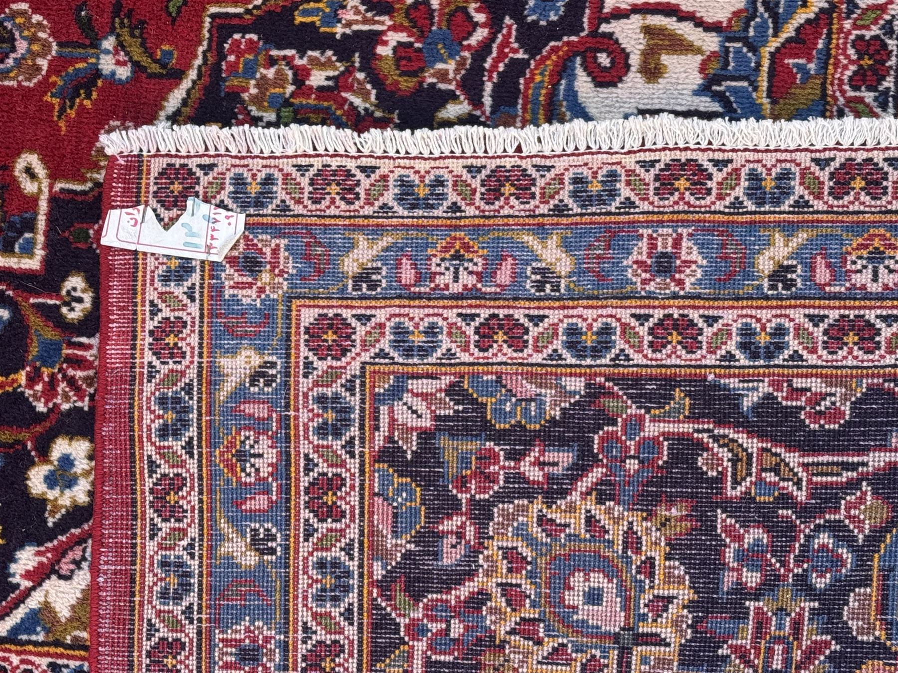 Large Kashan crimson ground carpet, central indigo medallion with stylised floral motifs, flanked by matching spandrels, bordered by multiple bands featuring repeating foliate and floral designs throughout