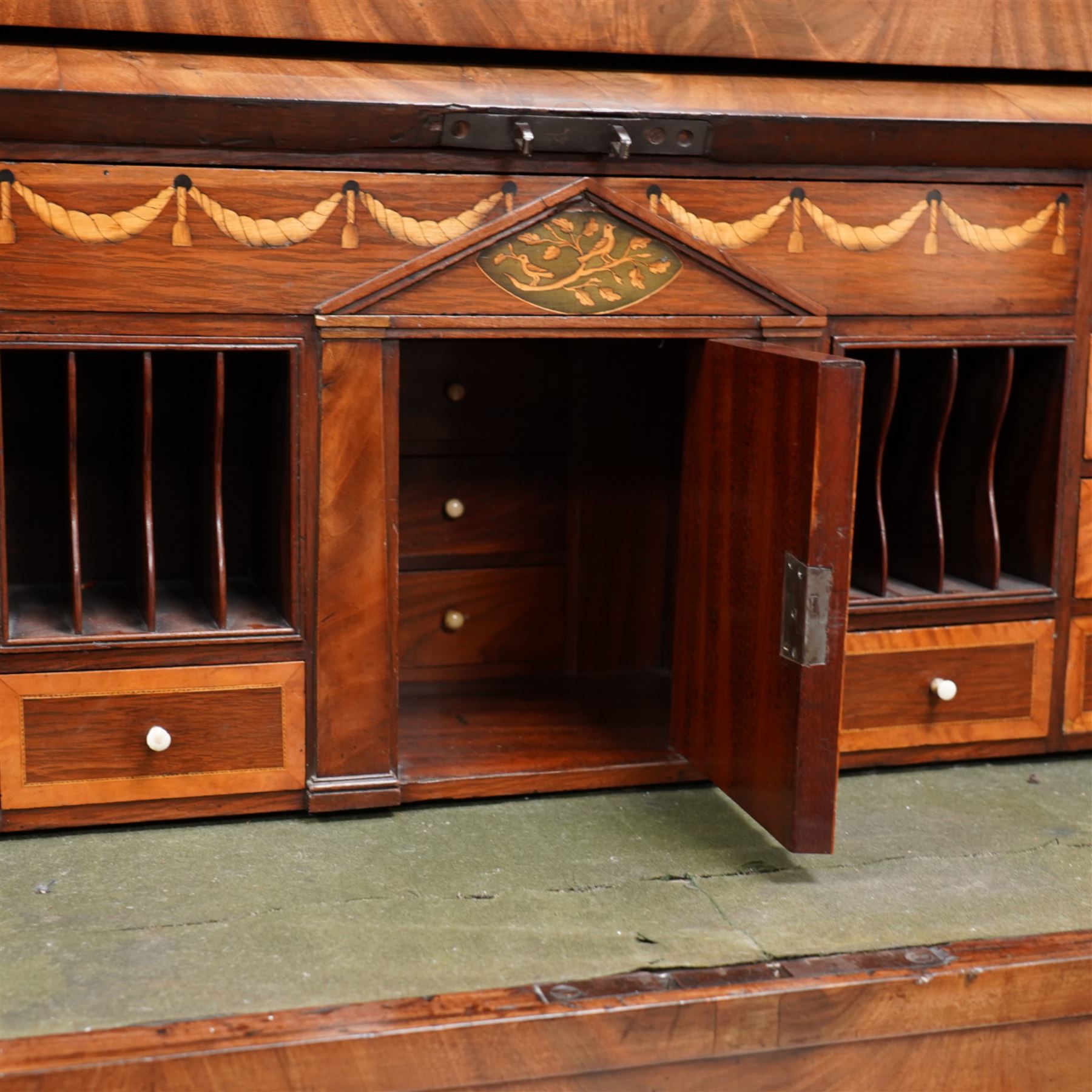 19th century Biedermeier figured mahogany cylinder bureau cabinet, the raised super structure with stepped pointed pediment over hidden cupboard and hinged fall front, the interior fitted with pigeonholes and secret drawers behind rusticated inlay, curved flanking cupboards fitted with internal drawers, the cylinder top opens to reveal small drawers, document divisions and secret compartments, sliding desk with central hinged writing surface, inlaid with satinwood bands and draped festoons, fitted with three long drawers, on bracket feet