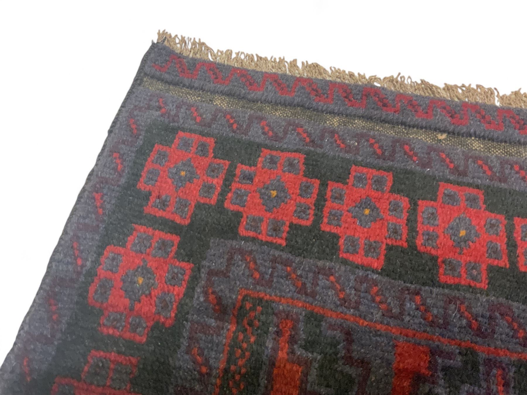 Baluchi indigo ground rug, the field decorated with all-over crimson and indigo lozenges, enclosed by geometric guard lines