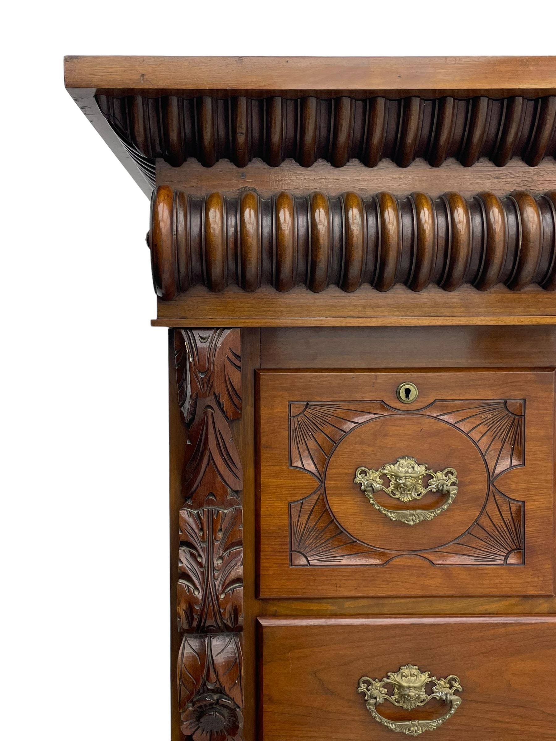 Late Victorian walnut Scotch chest, projecting cornice with turned quarter column mounts over matching half column to frieze, fitted with two upper short drawers with central cupboard, bevelled mirror glazed cupboard door, four graduating drawers below, foliage and flower head carved brackets to the uprights, panelled sides, chamfered plinth on turned feet