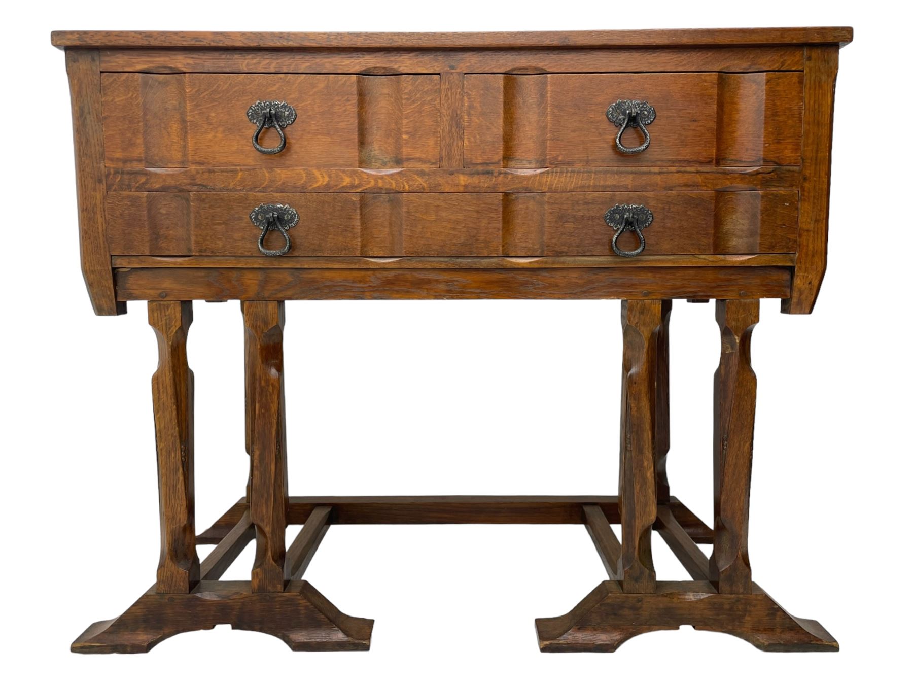 Arts & Crafts design oak chest on stand, rectangular top over two short and one long drawer, on a series of shaped and tapered supports with carved and beaded decoration, united by chamfered stretchers rails, on sledge feet 