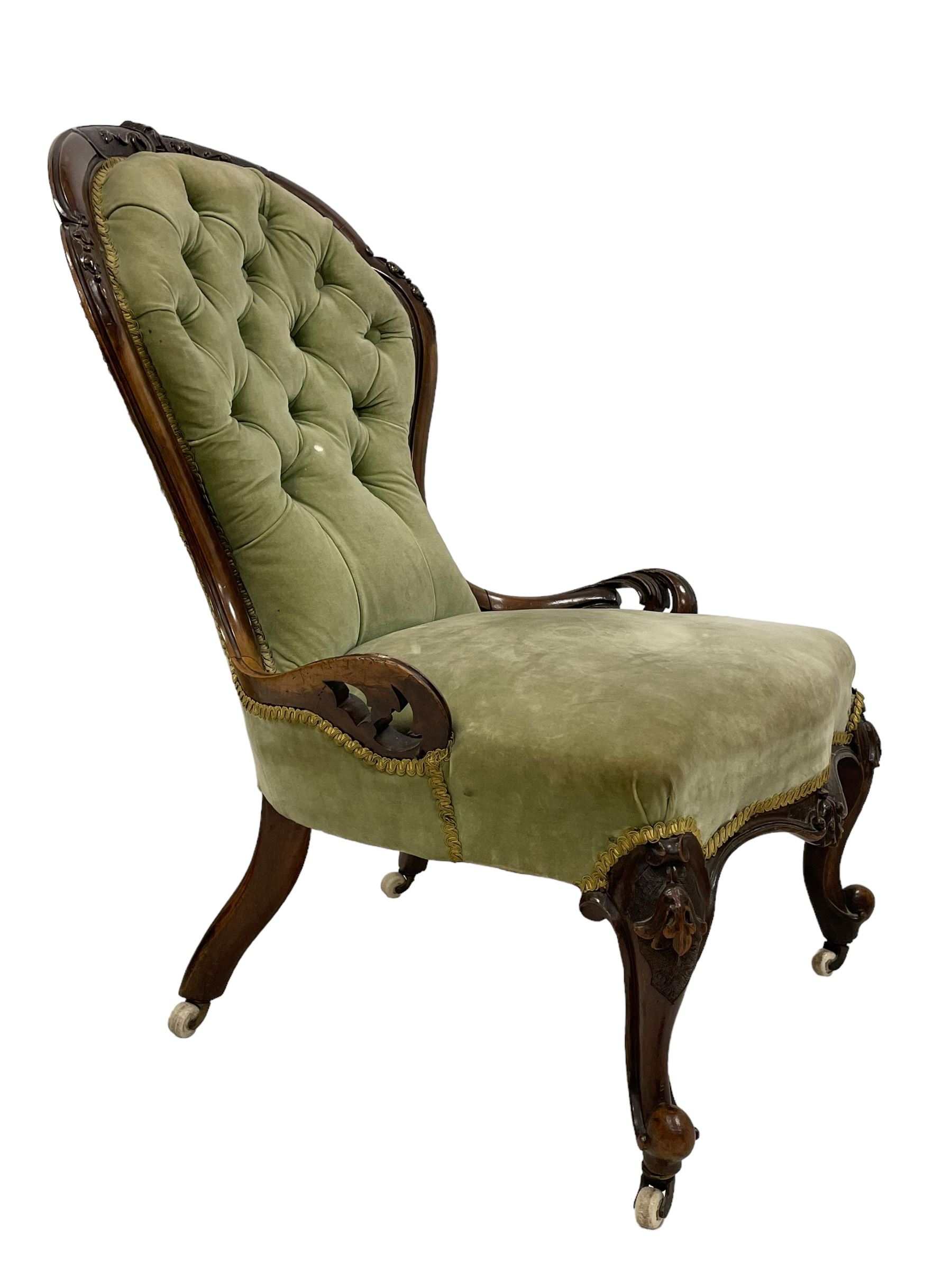 Pair of lady's and gentleman's Victorian carved walnut armchair and nursing chair, foliate carved cresting rail over shaped back with scrolled acanthus carved sides, the armchair with scroll arm terminals, the spoon back and sprung seat upholstered in buttoned sage green velvet, raised on cabriole supports with bell-flower moulded knees and scroll feet, on ceramic castors