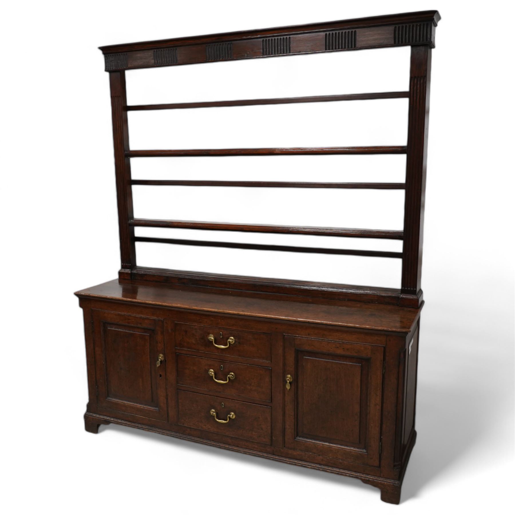 George III oak dresser, rectangular top, fitted with three central graduating cock-beaded drawers, flanked by panelled cupboards with quarter-canted pilaster uprights, lower moulded edge on bracket feet; with associated stained pine plate rack, carved with fluted detail (W170cm H124cm)