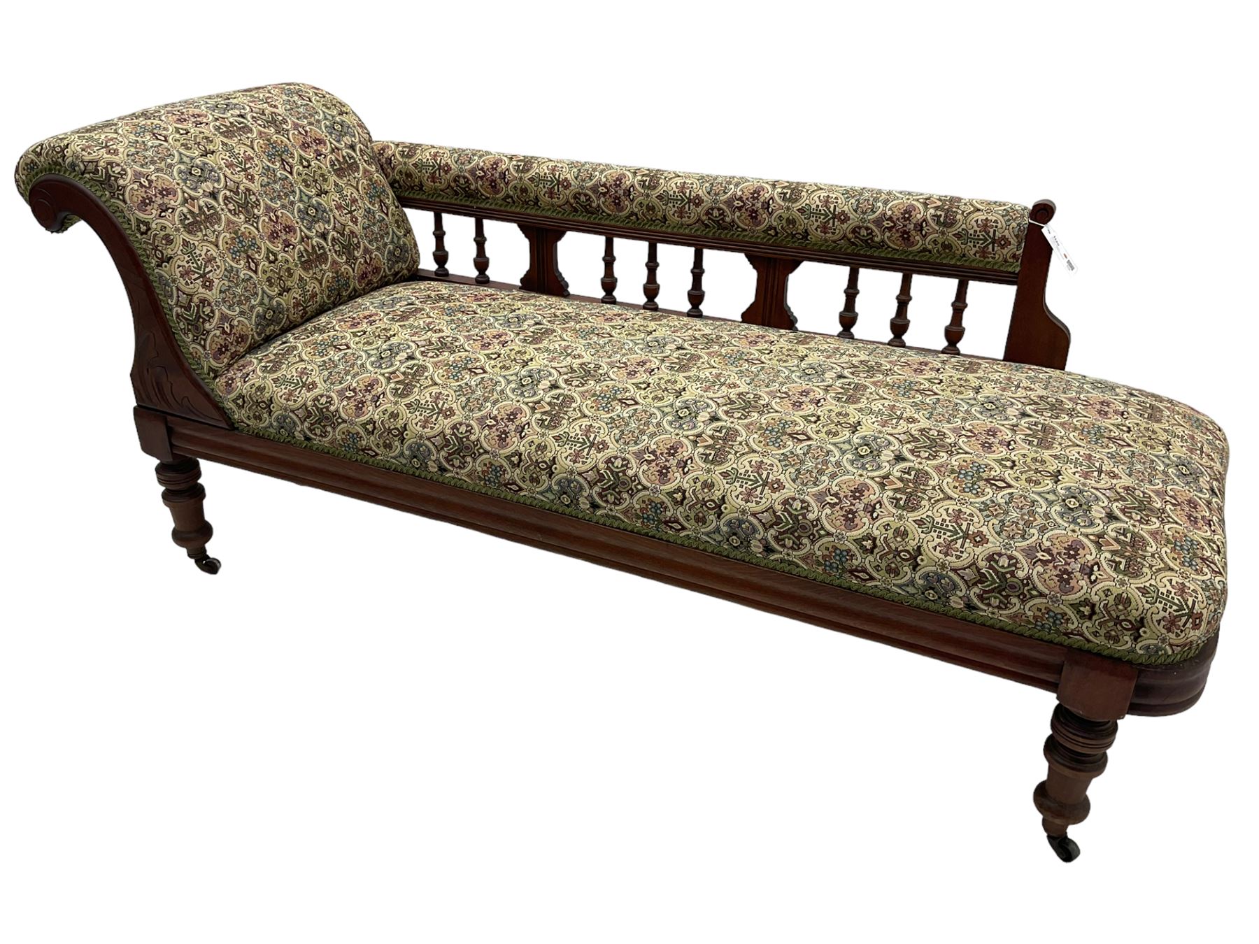 Late 19th century walnut framed chaise longue, upholstered in floral pattern fabric, rolled back rest and turned balustrade back, on turned feet with brass and ceramic castors 