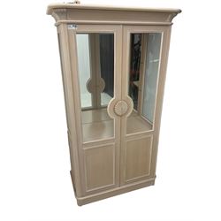 Contemporary display cabinet, moulded cornice above glazed panelled doors with central carved sunburst handles, mirrored back interior with lighting, lower enclosed storage compartment, raised on plinth base