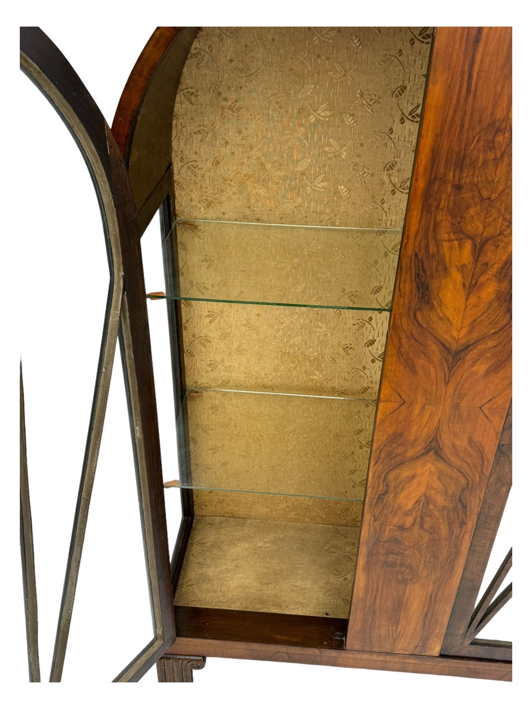 Early 20th century Art Deco walnut display cabinet, with arched top and carved floral crest, central band flanked by two glazed panel doors with decorative mullions, enclosing two glass shelves, on scroll carved bracket feet