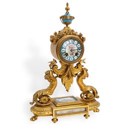 French-mid 19th century 8-day gilt and porcelain mantle clock with a break front plinth raised on paw feet, with recessed rectangular porcelain panels depicting two lovers and floral decoration, drum cased movement with a porcelain dial supported on two matching scroll supports, surmounted with a tapered porcelain urn and gilt finial, dial with cartouche Roman numerals on a blue ground and a depiction of cupid to the dial centre, twin train rack striking movement, striking the hours and half hours on a bell. With Pendulum and key.