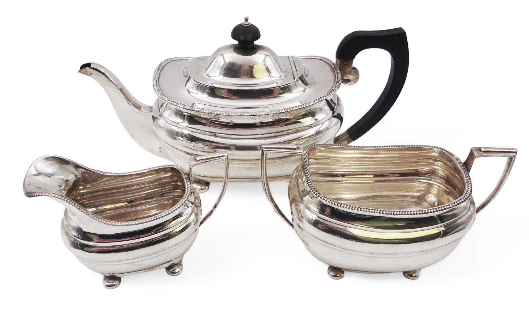 Silver three piece tea service, comprising teapot, twin handled open sucrier and a milk jug, all of oval part fluted form and upon four bun feet, the teapot with black plastic handle and finial, hallmarked S Blanckensee & Son Ltd, Chester 1930, teapot H16cm