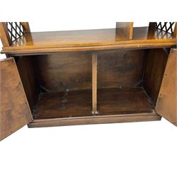 Mid 20th century oak bookcase cupboard, projecting cornice over three open shelves with subdivided sections and latticework uprights, two doors to the base with floral and scrollwork carvings and central brass handles, resting on a moulded plinth base