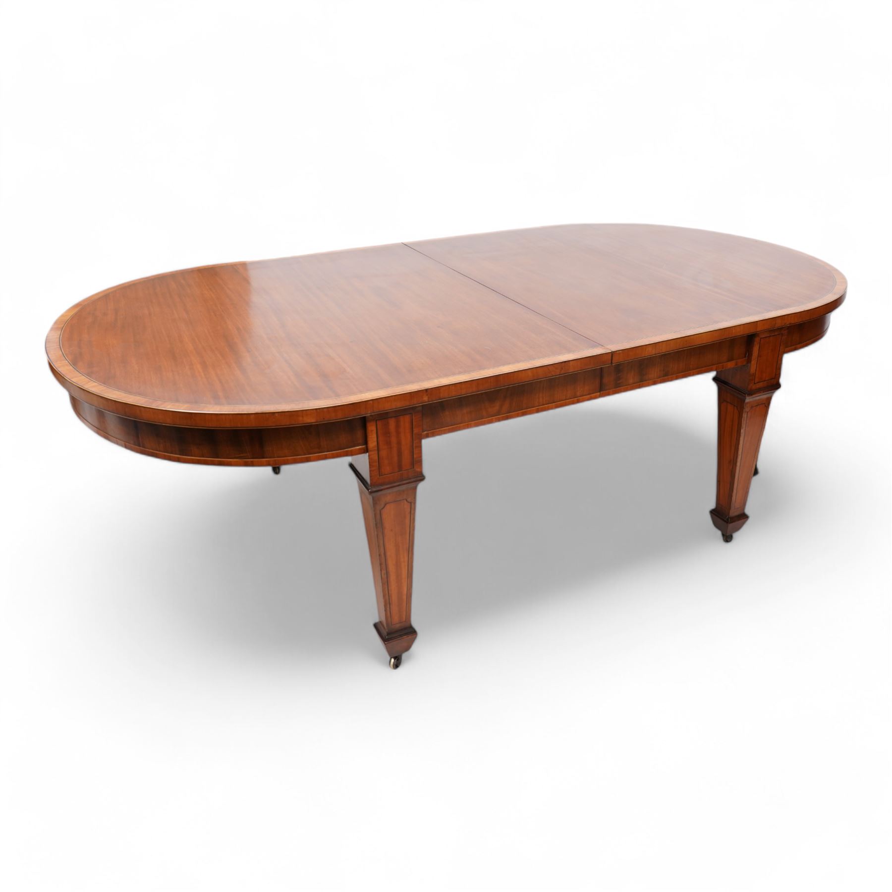 Late 19th to early 20th century mahogany and satinwood banded dining table, telescopic extending action, with three additional leaves, figured frieze rails over square tapering supports with spade feet, inlaid with satinwood panels, on brass castors 