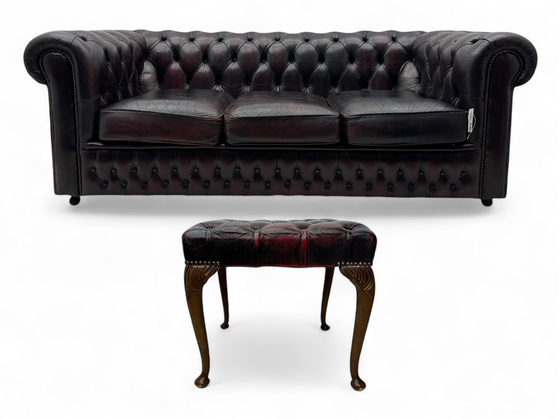 Chesterfield three-seat sofa, traditional shaped upholstered in deeply buttoned dark red leather; together with similar footstool 