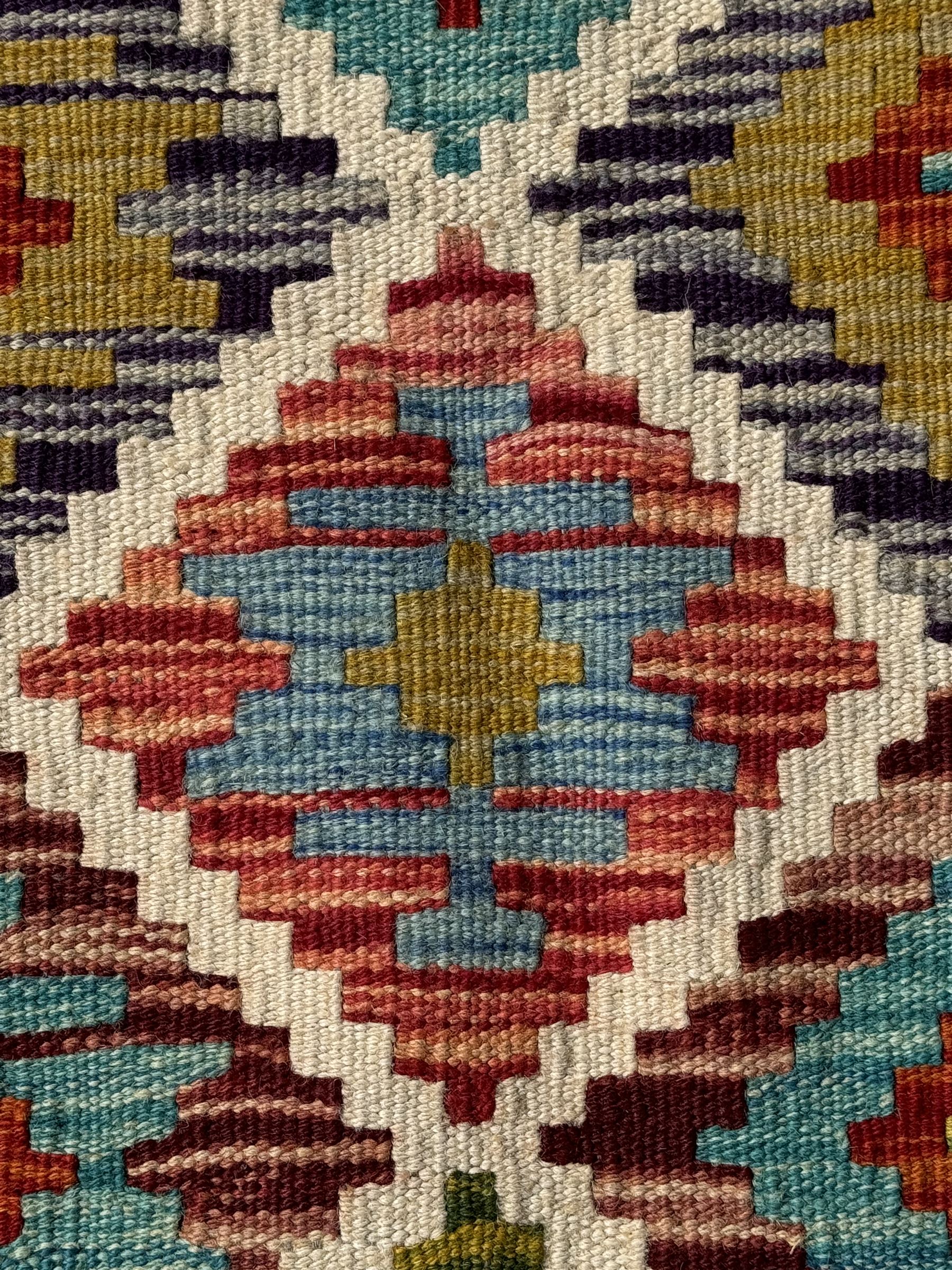 Chobi Kilim ground runner, the field decorated with a geometric pattern of coloured diamonds and triangles, each containing stylised motifs, the shorter ends enclosed by a plain border, and the longer sides with a multicoloured border

