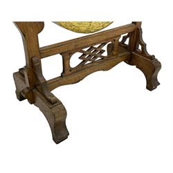 Early 20th century oak gong stand with gong and hammer, shaped cresting rail over moulded upper edge on shaped supports, hanging brass drum gong over fretwork middle rail, on raised platforms terminating to splayed feet