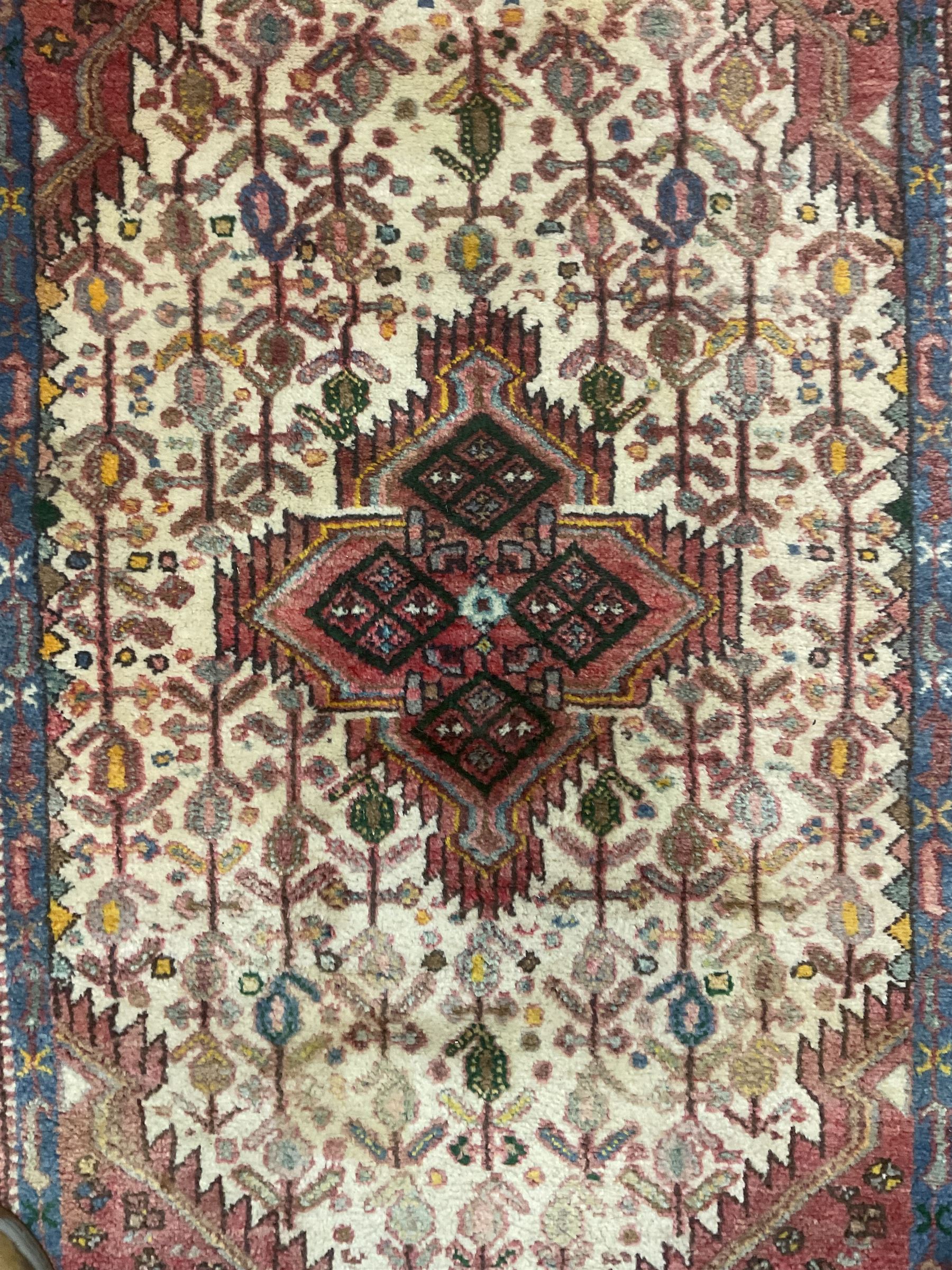 Small Persian rug, ivory and pale red ground, decorated with central medallion within a field of trailing Boteh motifs, geometric design guarded border