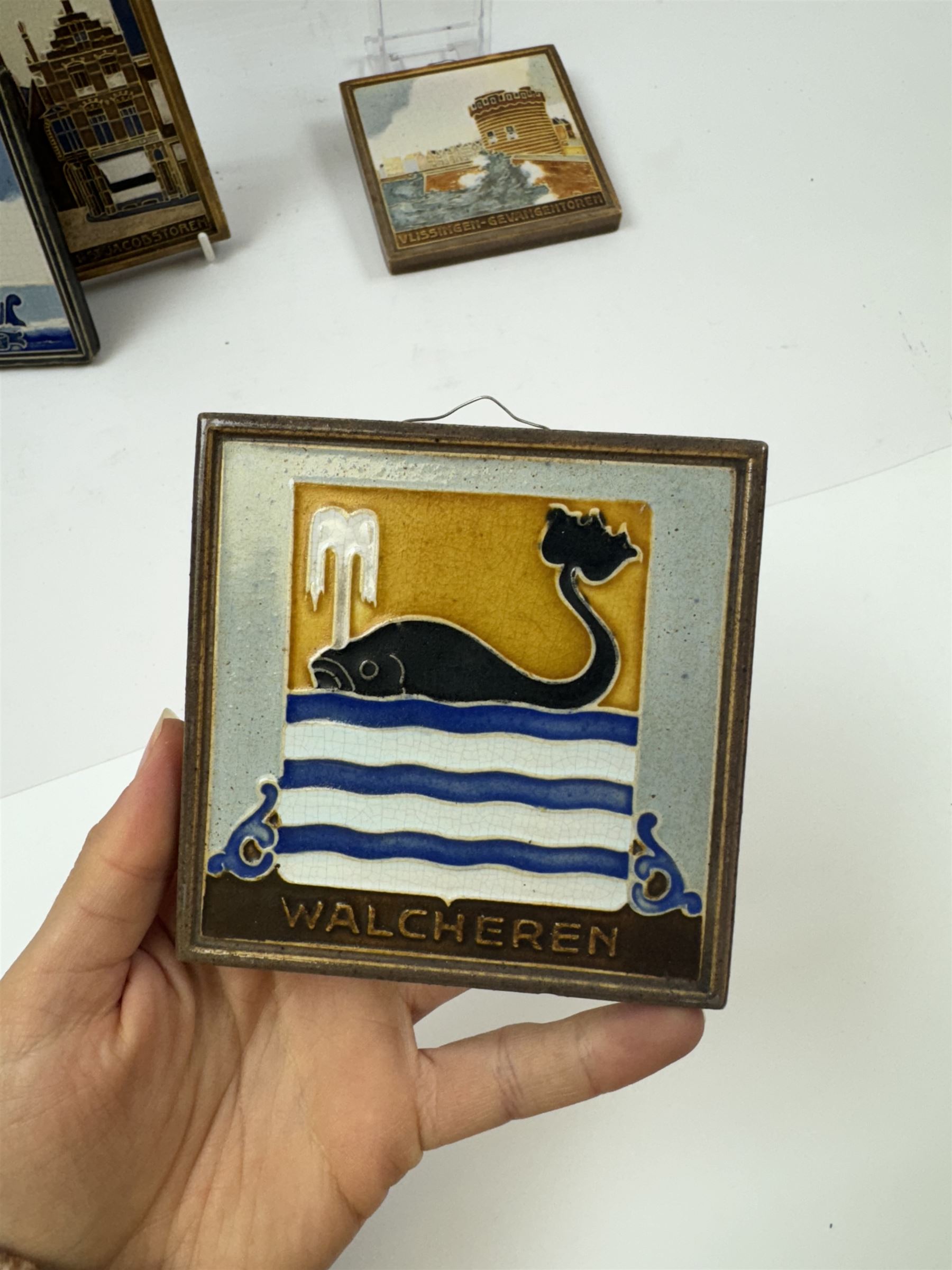 Five Dutch Westraven tiles, to include four square examples depicting maritime and similar scenes, and a rectangular example depicting a village scene, square tiles 10cm x 10cm, rectangular tile 15cm x 10cm