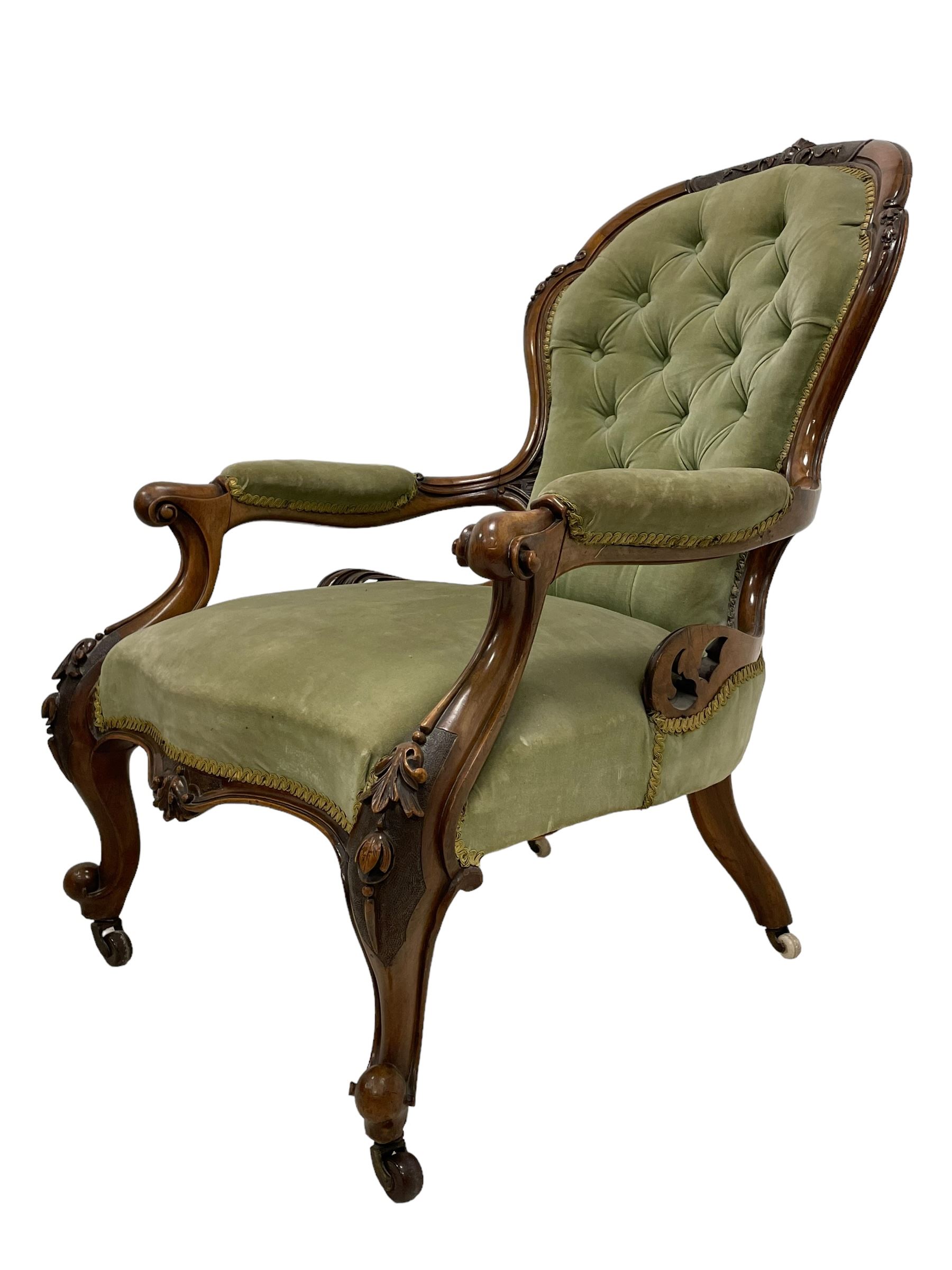 Pair of lady's and gentleman's Victorian carved walnut armchair and nursing chair, foliate carved cresting rail over shaped back with scrolled acanthus carved sides, the armchair with scroll arm terminals, the spoon back and sprung seat upholstered in buttoned sage green velvet, raised on cabriole supports with bell-flower moulded knees and scroll feet, on ceramic castors