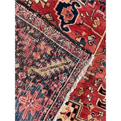 Persian Heriz red ground carpet, large central eight point medallion with projecting palmettes surrounded by small geometric motifs, decorated profusely with hooks, rosettes and animals, the busy border decorated with stylised foliate motifs within guard stripes 