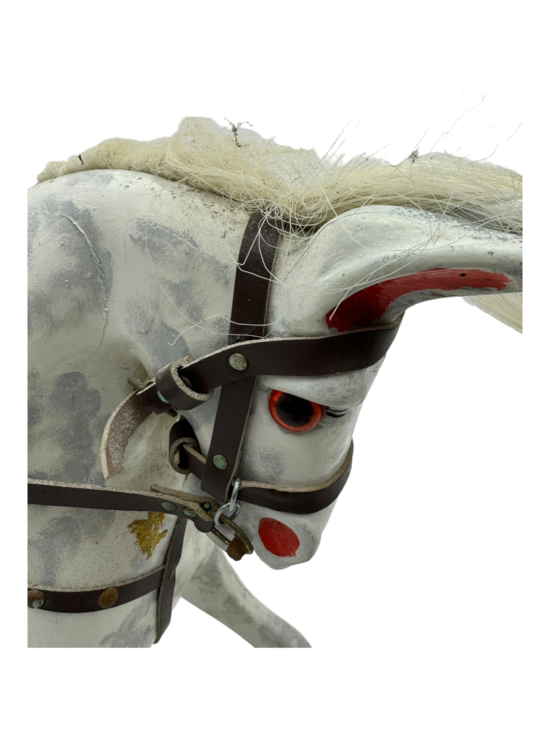 Mid 20th century rocking horse, dappled grey painted horse with applied mane and tail, red leather saddle and bridle accented with brass studs, supported by a stained wooden frame with turned supports and iron brackets, mounted on rockers