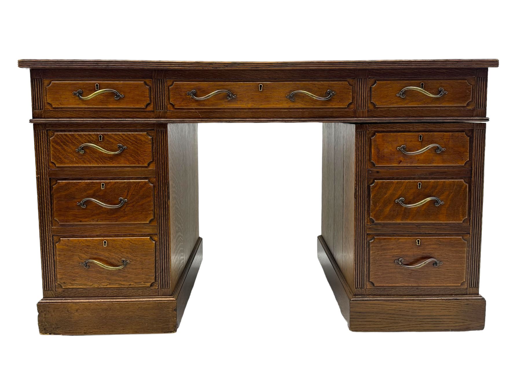 20th century oak twin pedestal desk, rectangular top with inset leather writing surface, fitted with nine drawers with chamfered edges to the raised panels, each with curved brass handles with scroll ends and keyholes, fluted detailing to the top and between the drawers, on moulded plinth base with castors