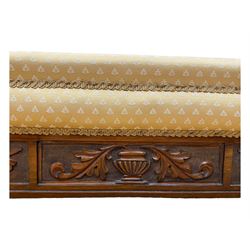 Late Victorian walnut framed chaise longue, scrolled backrest and sides upholstered in patterned yellow fabric, carved floral motifs to the backrest and sides, raised on turned supports with castors