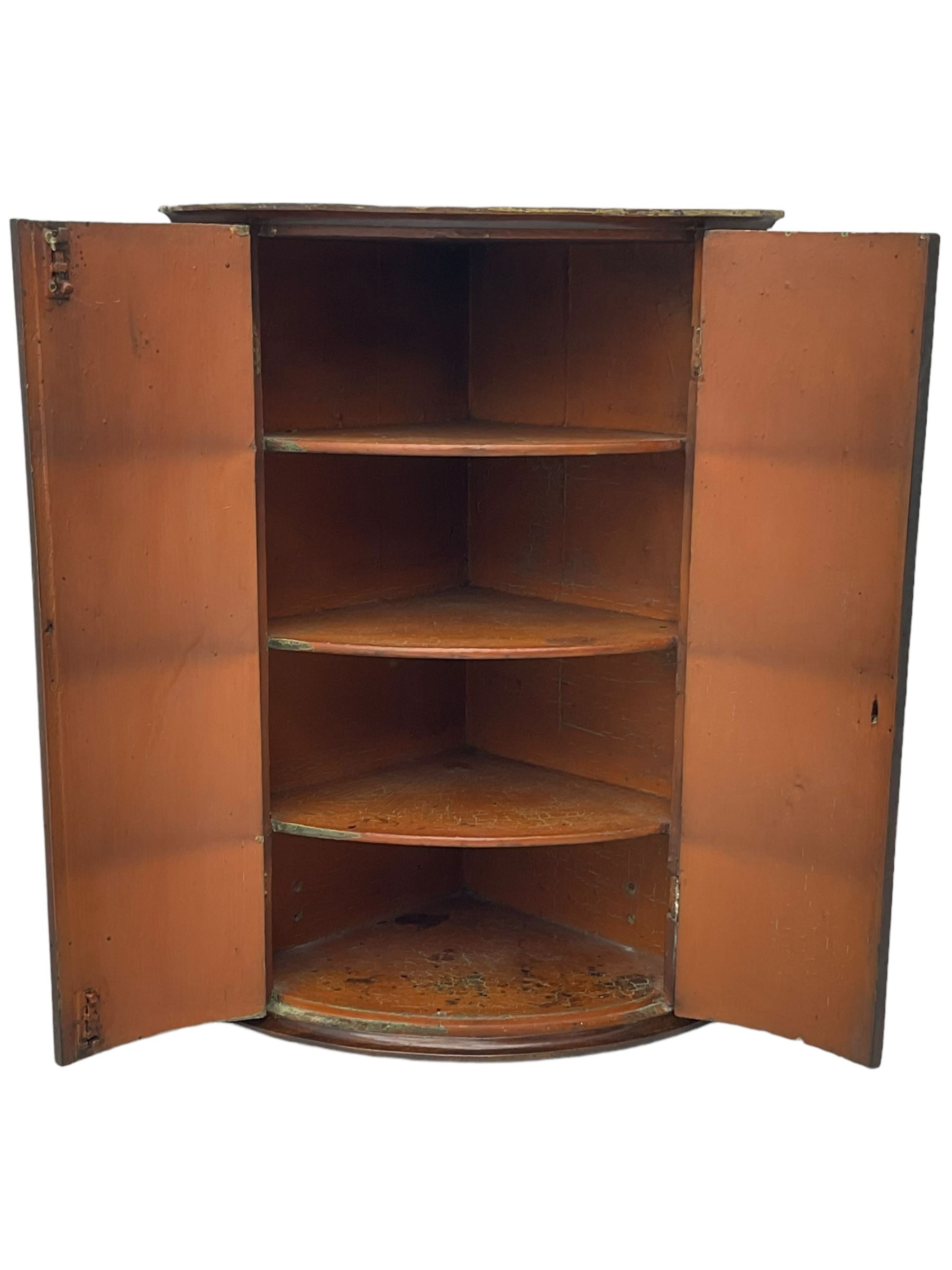 George III mahogany bow-front corner cupboard, enclosed by two figured doors with brass hinges and escutcheon, the painted interior fitted with three shelves 