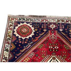 Persian Quashqai crimson ground rug, central geometric lozenge medallion surrounded by stylised plant motifs, indigo spandrels with further geometric designs, enclosed by an ivory border