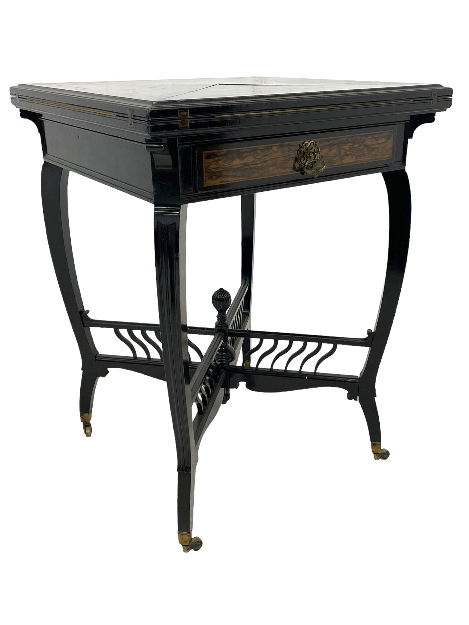 Late Victorian Coromandel wood and ebonised envelope card table, moulded swivel quadruple hinged top enclosing baize lined interior with sunken counter wells, fitted with single frieze drawer with Coromandel fascia and ornate cast handle, on four shaped and moulded supports terminating to square tapering feet, united by X-framed balustraded cross stretchers with reeded finial, on brass cups and castors 